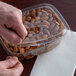 A hand opening a Dart deli container of almonds.