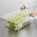 A person using a Cambro clear plastic container with a colander pan to hold lettuce.