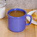 A peacock blue GET plastic mug filled with brown liquid on a table with pastries.