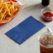 A basket of french fries and a blue napkin next to a drink.