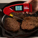 A hand using a Cooper-Atkins red digital thermometer to check the temperature of frying meat.