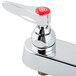 A close-up of a chrome T&S deck mounted faucet with a red button on top.