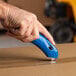 A hand using a Pacific Handy Cutter blue safety cutter to cut a box.