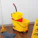 A Rubbermaid yellow mop bucket with red dirty water bucket and mop stand in a kitchen.