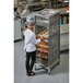 A woman in a white shirt and black pants putting trays of pastries on a Cambro sheet pan rack.