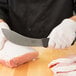 A person in white gloves using a Victorinox Butcher/Skinning Knife to cut meat on a cutting board.