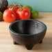 A black Polypropylene Perfecto Molcajete on a table with tomatoes and avocado.