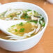 A white GET Water Lily melamine bowl filled with soup, noodles, and green onions.