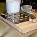 A Wilton rimless steel cookie sheet with cookies on a cutting board next to eggs and flour.