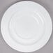 A close-up of an Arcoroc white porcelain saucer with a white rim on a gray surface.