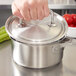 A hand using a Vollrath stainless steel pot lid to cover a pot.