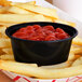 A black oval plastic souffle cup filled with ketchup on french fries.