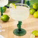 A Libbey cactus margarita glass with a drink and a lime wedge on the table.