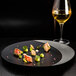 A RAK Porcelain silver and black flat plate with food and a glass of wine on a table.