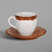 A white and brown RAK Porcelain espresso cup and saucer on a brown surface.