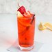A Stolzle highball glass filled with orange liquid with strawberries and lemons on the rim.