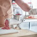 A person using a Weston manual meat grinder to grind meat on a table.