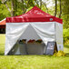 A red Backyard Pro canopy tent set up on grass with white side walls.