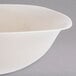 A close-up of a Fineline ivory plastic bowl with a curved edge on a grey surface.