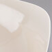 A close-up of a Fineline ivory plastic bowl with a white surface