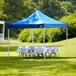 A blue Backyard Pro Courtyard canopy set up over a table with a white tablecloth on grass