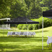 A black Backyard Pro Courtyard Series canopy with white tablecloths and white folding chairs set up in a grassy area.