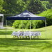 A table with a white tablecloth set up under a navy Backyard Pro Courtyard canopy on grass.