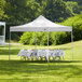 A white Backyard Pro Courtyard Series canopy over tables and white folding chairs set up in a grassy area.