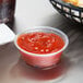 A plastic Dart souffle container of ketchup on a table with french fries.