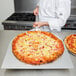 An American Metalcraft chef using an aluminum pizza peel to remove a pizza from the oven.