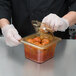 A person in gloves using a Cambro H-Pan lid to cover a plastic container of food.