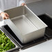 A person holding a Vollrath stainless steel steam table spillage pan with vegetables.