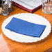 A navy blue Hoffmaster paper dinner napkin on a white surface on a table with a glass.