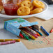 A box of Choice 24 Assorted Colors School Crayons on a table with a plate of food.