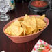 A large oval paprika polyethylene basket filled with tortilla chips on a restaurant table.