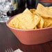 A paprika oval polyethylene basket filled with chips on a table in a Mexican restaurant.