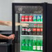 A man opening a Beverage-Air Marketeer series glass door refrigerator with bottles of soda.