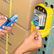A person's hand using a Pacific Handy Cutter BB-6017KIT box cutter on a box with a yellow button on the tool.