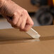 A hand holding a Pacific Handy Cutter knife cutting a box.