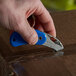 A person using a blue and silver Pacific Handy Cutter to cut a box.