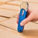 A hand holding a blue Pacific Handy Cutter S7 safety cutter over cardboard.