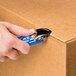 A person using a blue Pacific Handy Cutter to open a box.