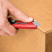 A person using a red Pacific Handy Cutter to open a box.