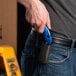 A hand holding a black and blue Pacific Handy Cutter clip-on holster.