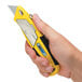 A hand holding a yellow and black Pacific Handy Cutter Metal Auto-Loading Utility Knife.