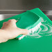 A hand using a green brush to clean a green cutting board.