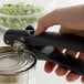 A person's hand using a black OXO handheld can opener to open a can.