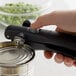 A hand using an OXO Good Grips handheld can opener to open a can.