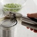A hand using an OXO SteeL handheld can opener to open a can.