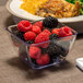 A Dinex clear SAN plastic bowl filled with blackberries and raspberries next to a plate of food.